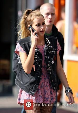 Alice Dellal leaves home wearing a pink dress, torn fishnet tights and a sleeveless denim jacket with a penis badge...