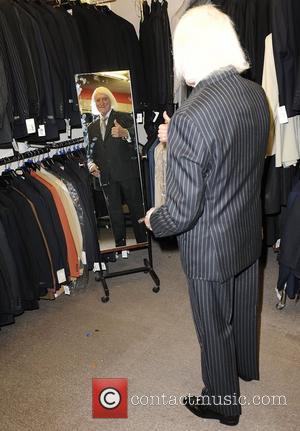 Sir Jimmy Savile tries on a suit at Warren Gold at Gold's Factory Outlet where he wore a suit to...